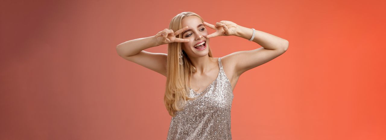 Femme souriante d'une trentaine d'années aux cheveux blonds mi-longs, tenue décontractée chic, portrait lumineux sur fond corail doux